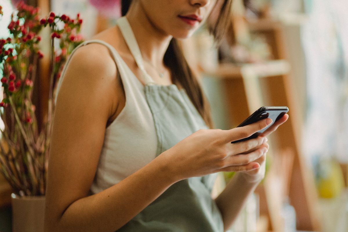 A florist checking her phone inside a small shop — photo by Amina Filkins on Pexels